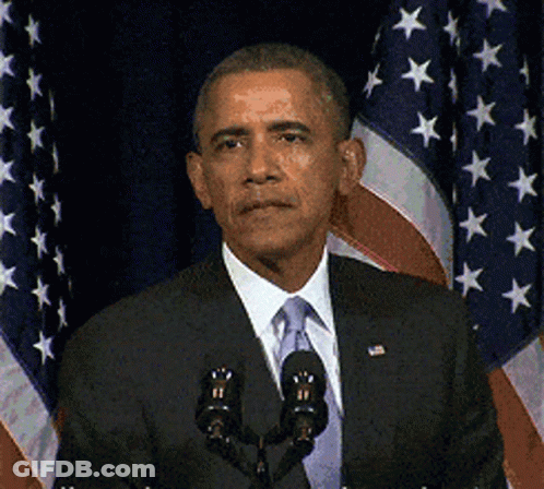 A Man In A Suit And Tie Is Speaking Into A Microphone In Front Of An American Flag GIF