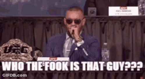 A Man In A Suit And Tie Is Speaking Into A Microphone While Sitting At A Table . GIF