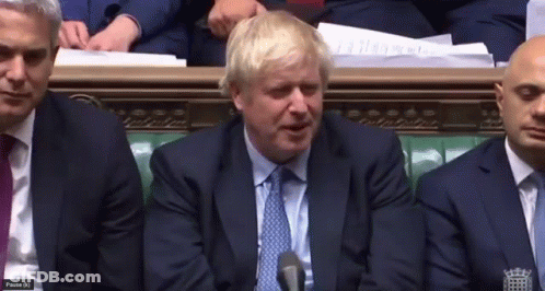 A Man In A Suit And Tie Is Speaking Into A Microphone While Sitting In A Room With Other Men GIF