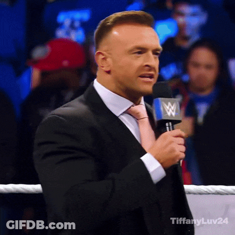A Man In A Suit And Tie Is Speaking Into A Microphone With A W Logo On It GIF