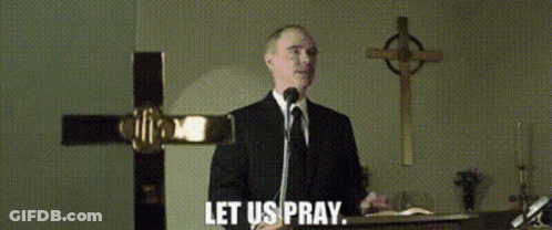 A Man In A Suit And Tie Is Speaking Into A Microphone With The Words Let Us Pray Below Him GIF