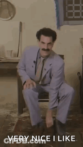 A Man In A Suit And Tie Is Squatting Down In A Room With The Words `` Very Nice I Like '' . GIF