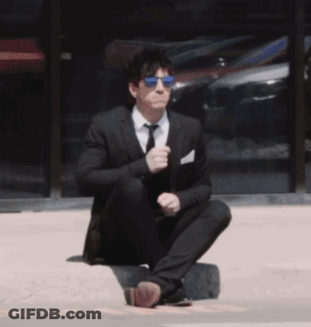 A Man In A Suit And Tie Is Squatting Down On The Ground GIF