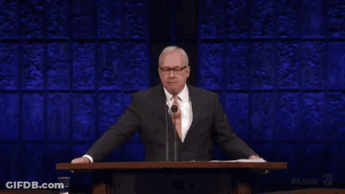 A Man In A Suit And Tie Is Standing At A Podium Giving A Speech And The Word Liar Is Above Him . GIF