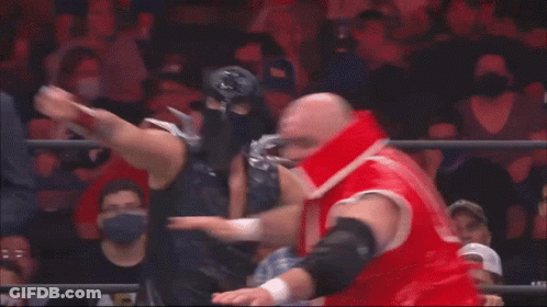 A Man In A Suit And Tie Is Standing Behind Two Wrestlers GIF