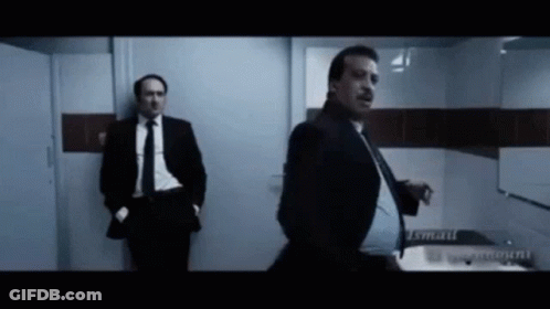 A Man In A Suit And Tie Is Standing In A Bathroom GIF