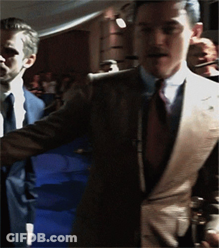 A Man In A Suit And Tie Is Standing In A Crowd GIF