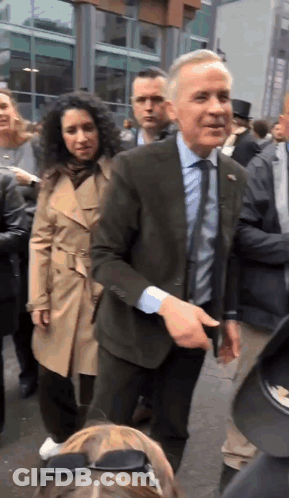 A Man In A Suit And Tie Is Standing In A Crowd Of People GIF