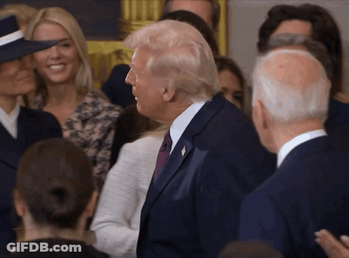 A Man In A Suit And Tie Is Standing In A Crowd GIF