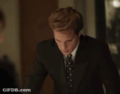 A Man In A Suit And Tie Is Standing In A Dark Room . GIF