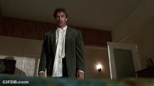 A Man In A Suit And Tie Is Standing In A Dark Room And Looking At The Camera . GIF