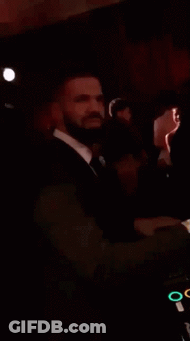 A Man In A Suit And Tie Is Standing In A Dark Room And Smiling . GIF