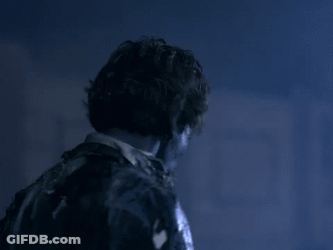 A Man In A Suit And Tie Is Standing In A Dark Room With A Blue Light Behind Him . GIF