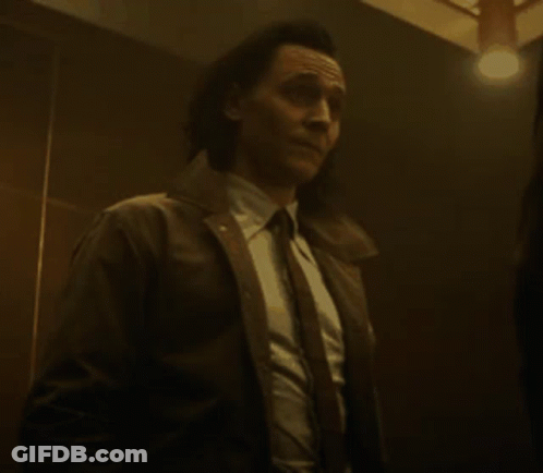 A Man In A Suit And Tie Is Standing In A Dark Room With A Light On . GIF