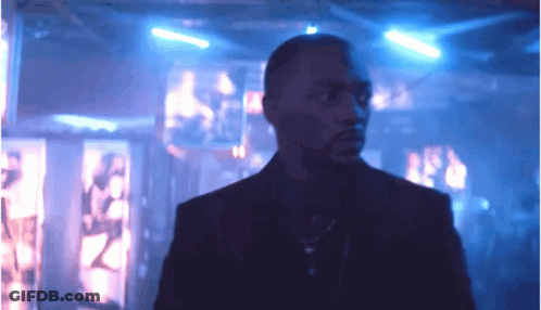 A Man In A Suit And Tie Is Standing In A Dark Room With Blue Lights GIF