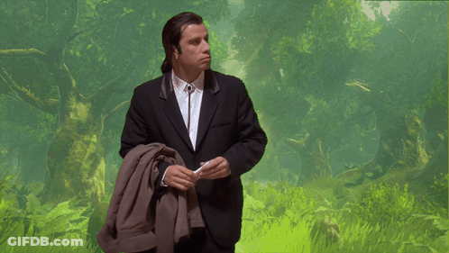 A Man In A Suit And Tie Is Standing In A Field GIF