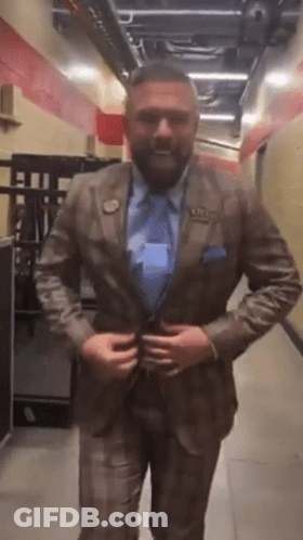 A Man In A Suit And Tie Is Standing In A Hallway Adjusting His Jacket GIF
