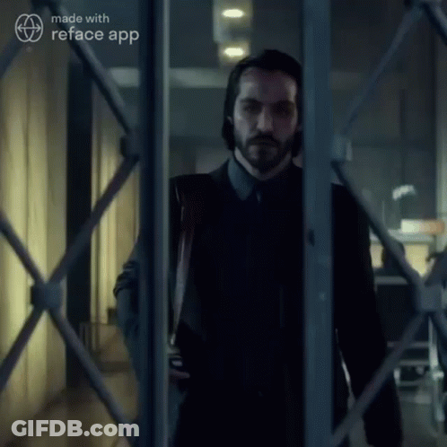 A Man In A Suit And Tie Is Standing In A Hallway Behind A Fence Made With Reface App GIF