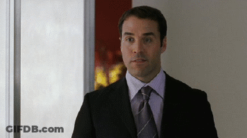 A Man In A Suit And Tie Is Standing In A Hallway GIF
