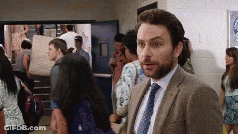 A Man In A Suit And Tie Is Standing In A Hallway Surrounded By Students . GIF