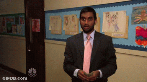 A Man In A Suit And Tie Is Standing In A Hallway With A Nbc Logo On The Wall GIF
