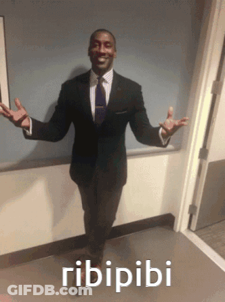 A Man In A Suit And Tie Is Standing In A Hallway With The Word Ribiribi Written On The Floor Below Him GIF