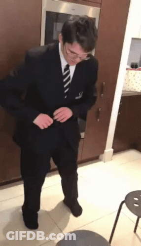 A Man In A Suit And Tie Is Standing In A Kitchen Adjusting His Jacket GIF