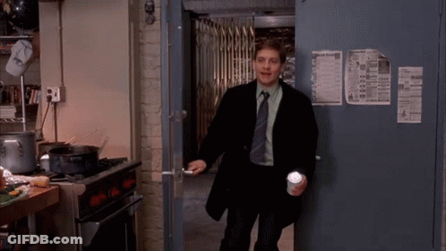 A Man In A Suit And Tie Is Standing In A Kitchen Holding A Cup And A Flashlight . GIF