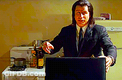 A Man In A Suit And Tie Is Standing In A Kitchen Holding A Laptop GIF