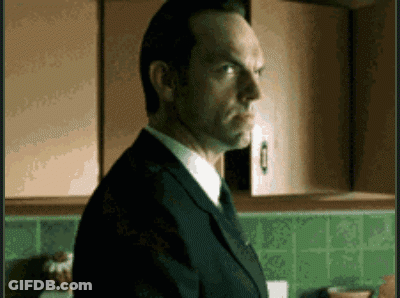 A Man In A Suit And Tie Is Standing In A Kitchen With Green Tiles GIF