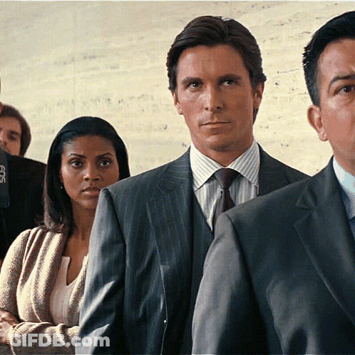 A Man In A Suit And Tie Is Standing In A Line With Other People GIF