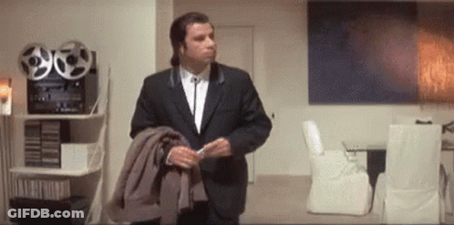 A Man In A Suit And Tie Is Standing In A Living Room Holding His Jacket . GIF
