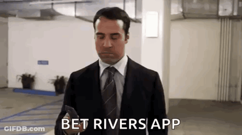 A Man In A Suit And Tie Is Standing In A Parking Garage And Looking At His Phone . GIF