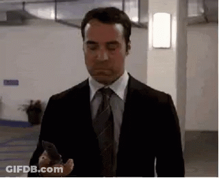 A Man In A Suit And Tie Is Standing In A Parking Garage Holding A Cell Phone . GIF