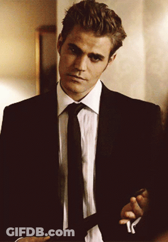 A Man In A Suit And Tie Is Standing In A Room GIF