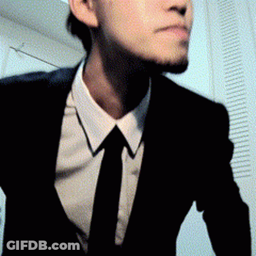 A Man In A Suit And Tie Is Standing In A Room GIF