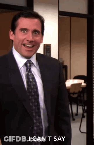 A Man In A Suit And Tie Is Standing In A Room And Smiling . GIF