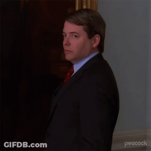 A Man In A Suit And Tie Is Standing In A Room . GIF