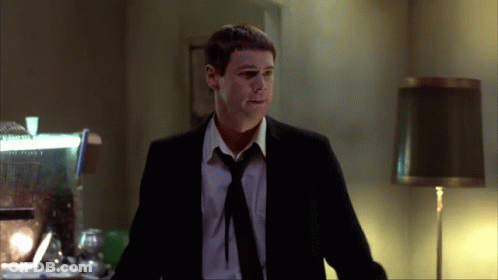 A Man In A Suit And Tie Is Standing In A Room GIF