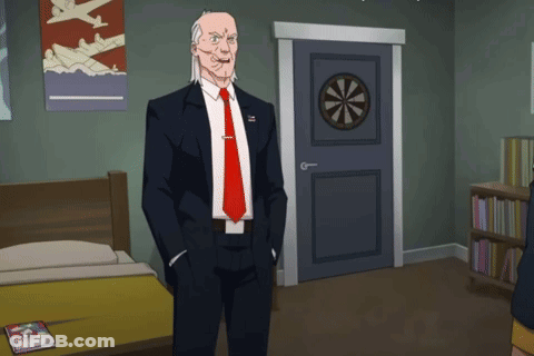 A Man In A Suit And Tie Is Standing In A Room With A Dart Board On The Door GIF