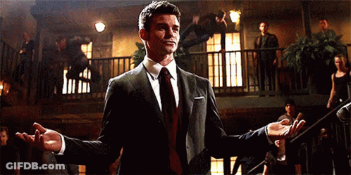 A Man In A Suit And Tie Is Standing In A Room With His Arms Outstretched GIF