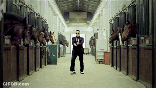 A Man In A Suit And Tie Is Standing In A Stable Surrounded By Horses GIF