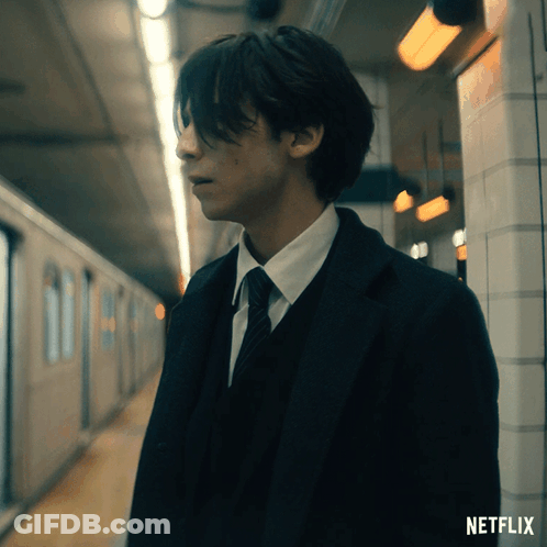 A Man In A Suit And Tie Is Standing In A Subway Station With A Netflix Logo Behind Him GIF