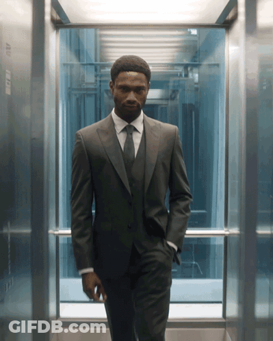A Man In A Suit And Tie Is Standing In An Elevator With His Hands In His Pockets GIF