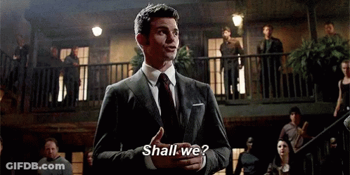 A Man In A Suit And Tie Is Standing In Front Of A Balcony Talking To A Crowd . GIF