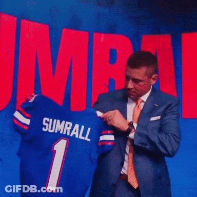 A Man In A Suit And Tie Is Standing In Front Of A Banner That Says Ump GIF