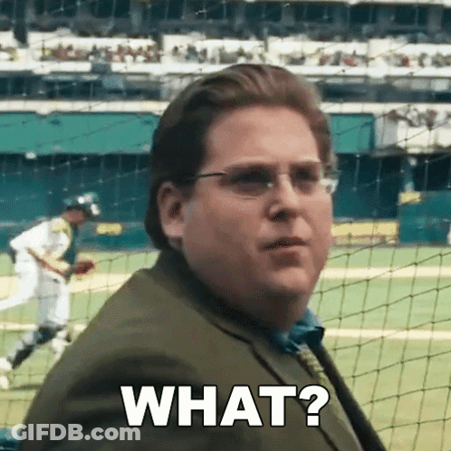 A Man In A Suit And Tie Is Standing In Front Of A Baseball Field And Asking What ? GIF