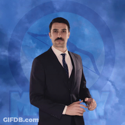 A Man In A Suit And Tie Is Standing In Front Of A Blue Background With The Letter M. GIF