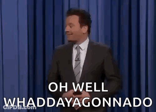 A Man In A Suit And Tie Is Standing In Front Of A Blue Curtain And Saying Oh Well Whaddayagonnado . GIF