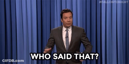 A Man In A Suit And Tie Is Standing In Front Of A Blue Curtain And Saying `` Who Said That ? '' GIF